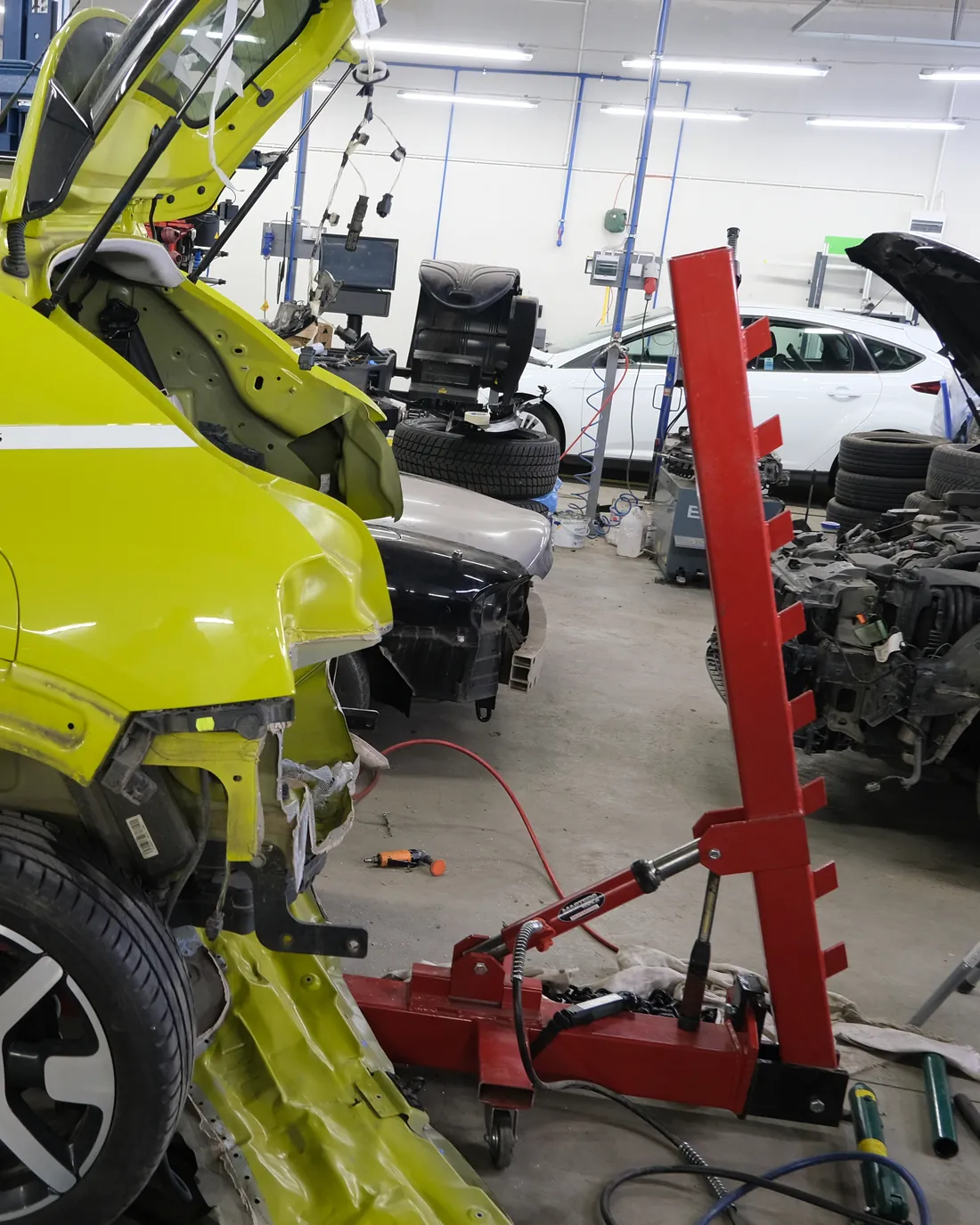 Żółte auto marki Citroen po kolizji, tyłem do kadru, przy czerwonej wieży ramy naciągowej w hali blacharskiej