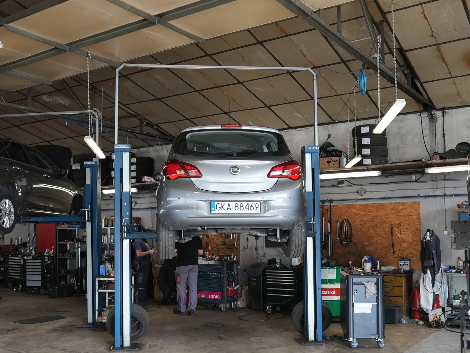 Hala serwisowa Bryksacar: srebrny Opel Corsa na podnośniku, pod autem dwóch mechaników