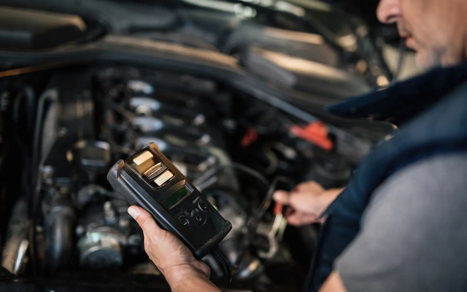 Mechanik trzyma ręczny tester podłączony do auta z otwartą maską